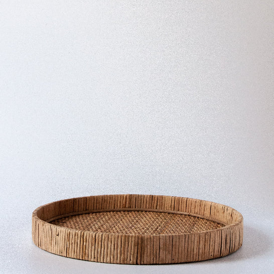A medium-sized rattan tray with a natural brown colour, featuring a flat surface and a cylindrical rim, placed against a neutral background - Anboise
